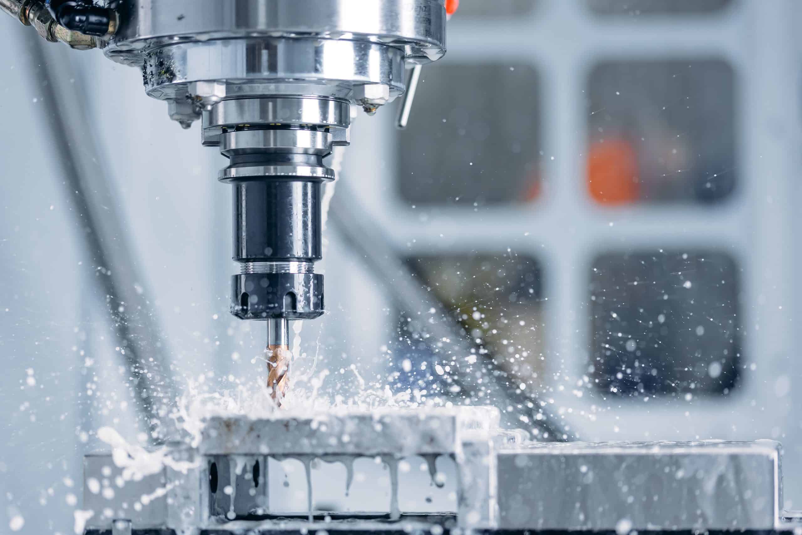 CNC milling machine cutting metal with coolant spraying around the tool.